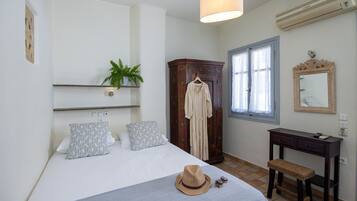 Un dormitorio con cama, armario, escritorio y una planta colgante.