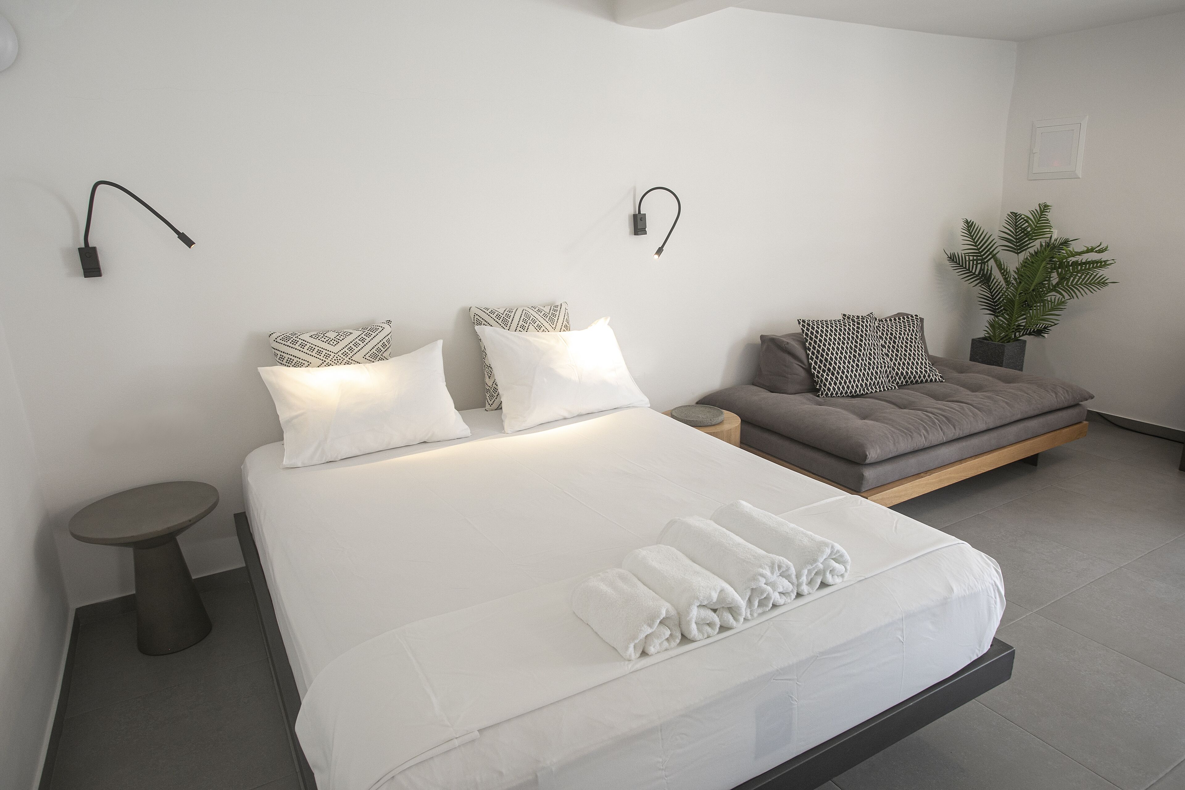 Ein modernes Schlafzimmer mit einem großen Bett, Nachttischen, einer Couch und einer Topfpflanze.
