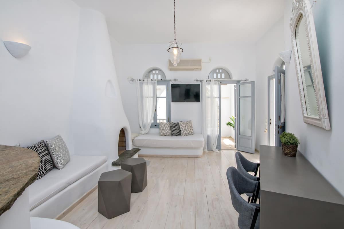 Quarto moderno e bem iluminado, com sofá branco, mesa de jantar e um espelho grande.