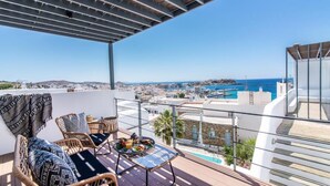 Ein Balkon mit Korbmöbeln, einem Tisch mit Getränken und Snacks sowie Blick auf das Meer und die Stadt.