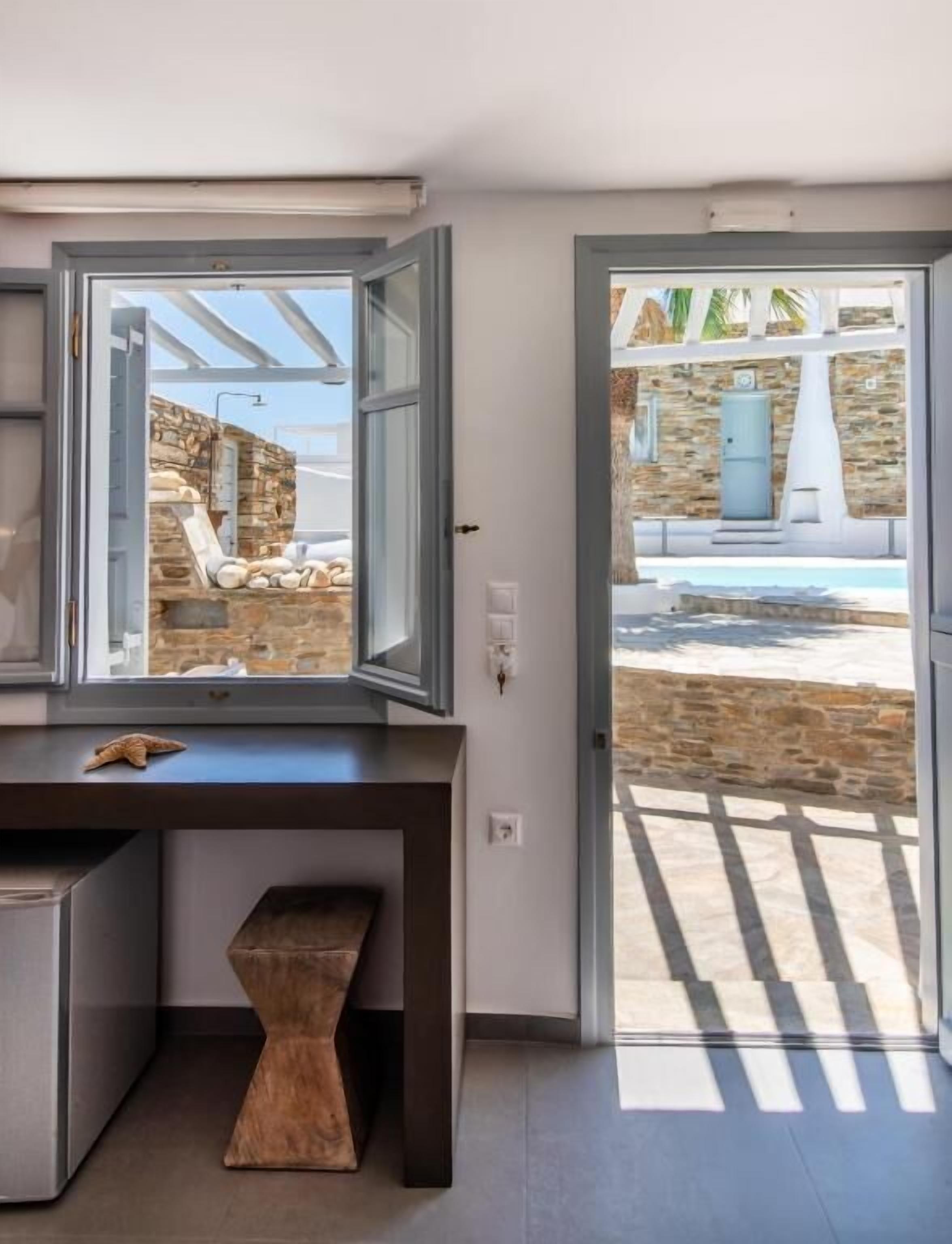 A modern kitchen with a large window, a built-in bench, and a view of a pool and stone wall outside.
