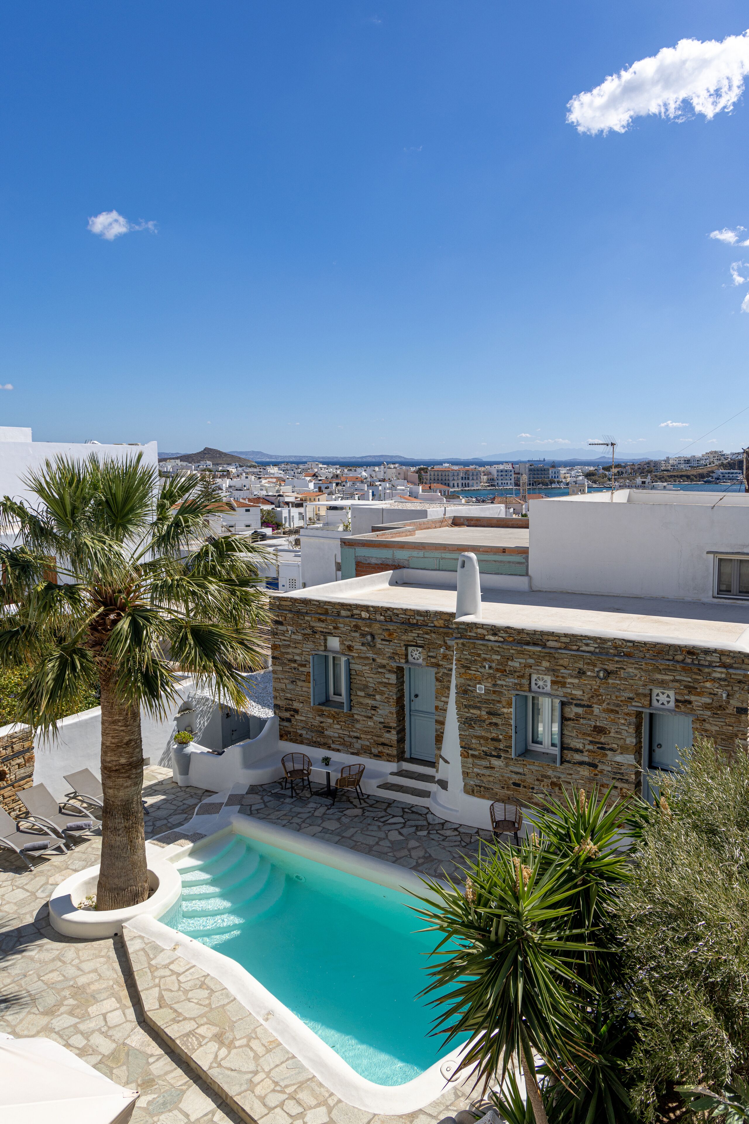 Una piscina en la azotea con un edificio de piedra, palmeras y vistas a la ciudad.