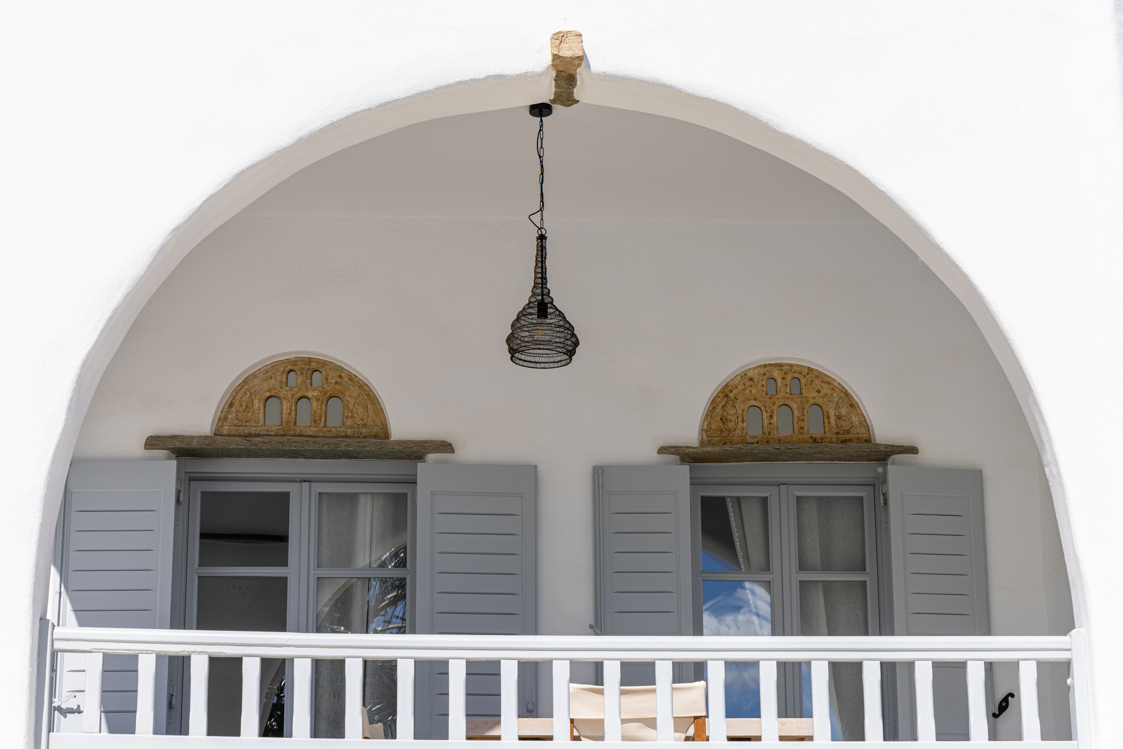 A balcony with white railings, grey shutters, and a hanging light fixture.