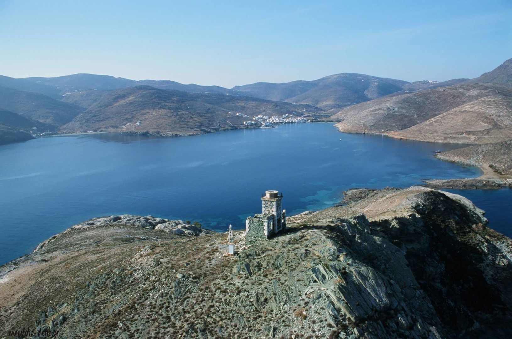 A coastal landscape with a clear view of a large body of water, rocky terrain, and a small tower structure.
