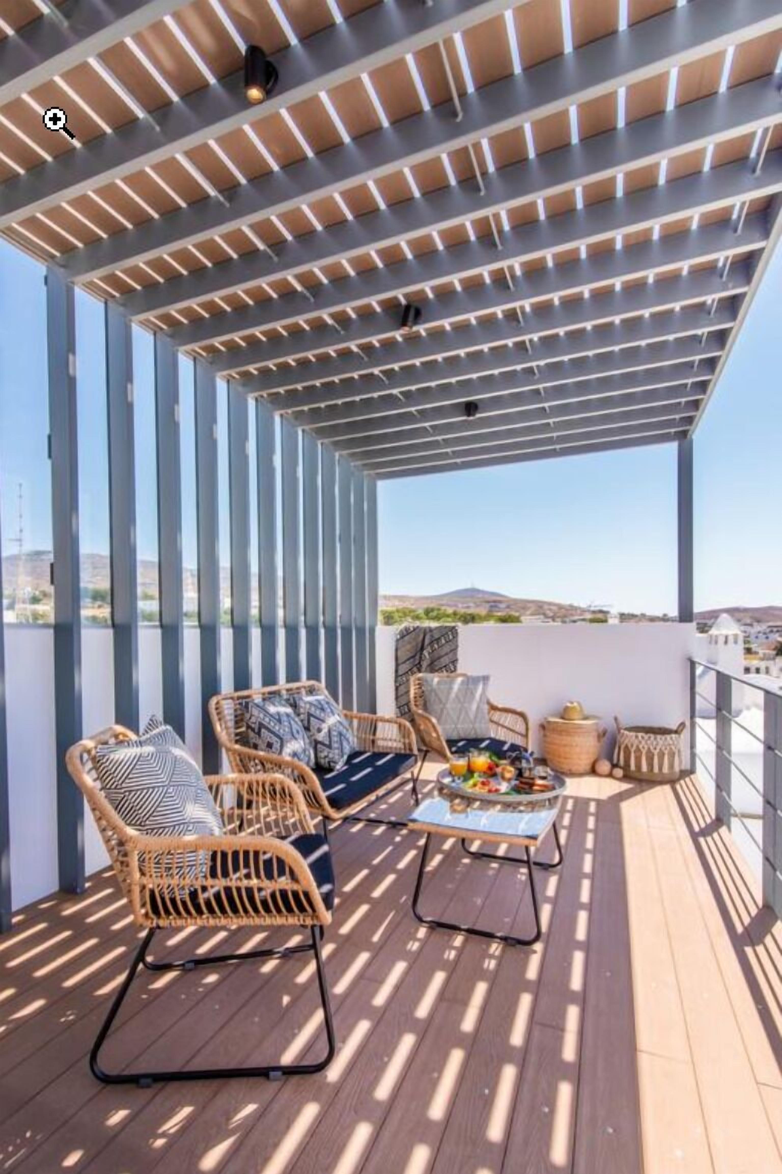 A covered outdoor seating area with wicker chairs and a table, overlooking a cityscape.