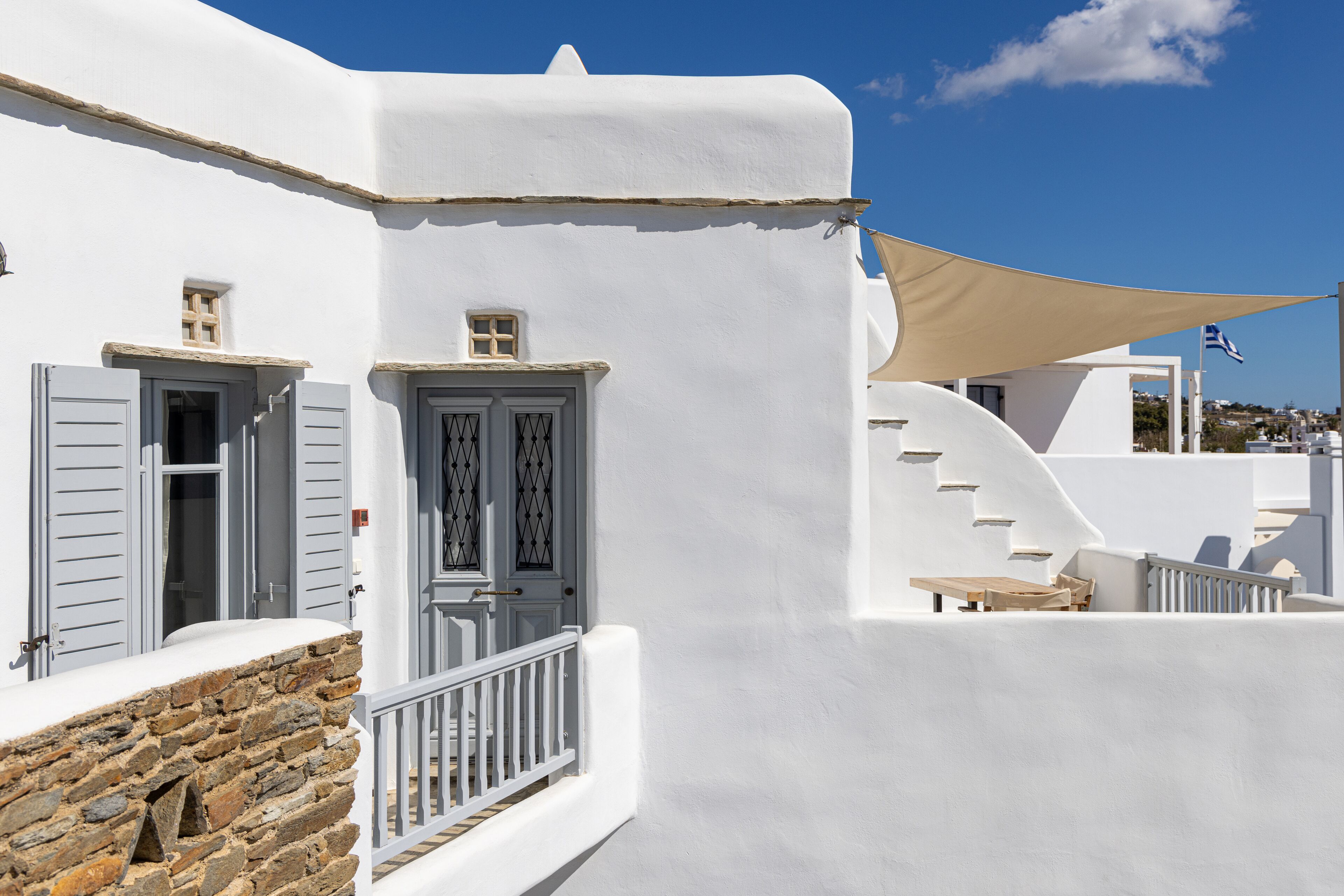 Een wit gebouw met grijze luiken, een stenen muur en een beige luifel.