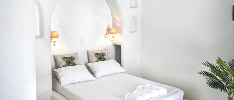 A modern bedroom with a large bed, a chandelier, and a potted plant.