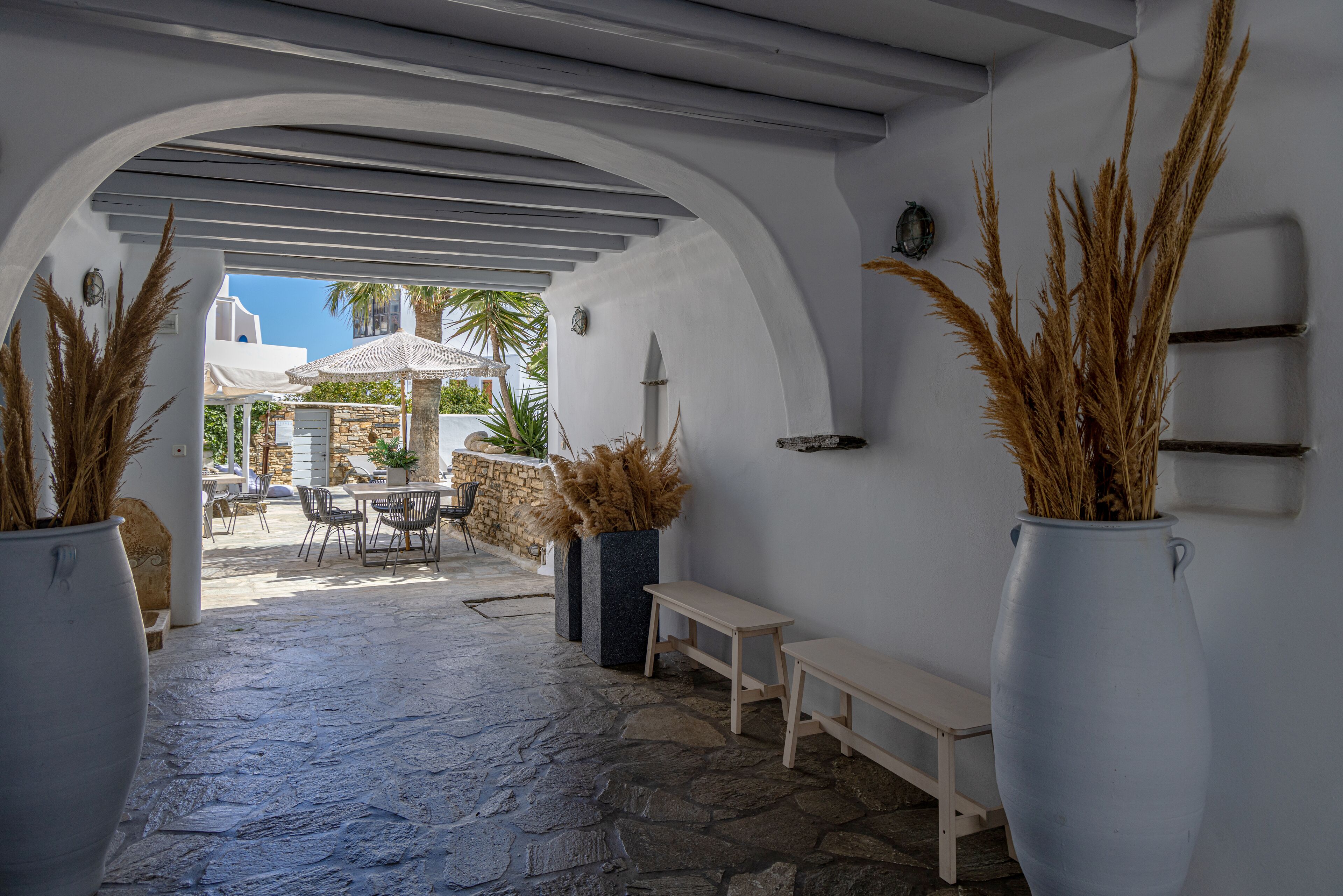 A stone-paved outdoor area with a white bench and a table under a white archway.