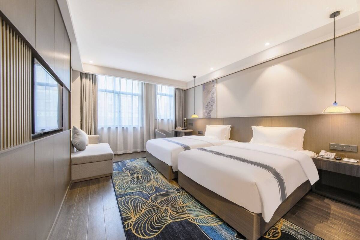 Habitación de hotel con dos camas, zona de estar, escritorio y ventana grande.