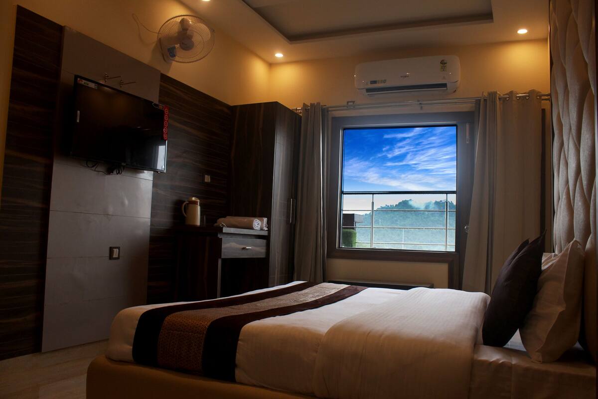Un cuarto de hotel con una cama grande, un televisor instalado en la pared, una ventana con vista al mar y un equipo de aire acondicionado.