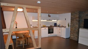 A modern kitchen with white cabinetry, a wooden dining table with chairs, and a stone accent wall. - Dorner Hof (Sibratsgfaell)