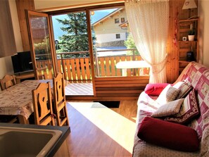 Une pièce chaleureuse avec un plancher en bois, un canapé agrémenté de coussins à motifs, une table à manger avec des chaises, et une porte-fenêtre coulissante donnant sur une terrasse extérieure.