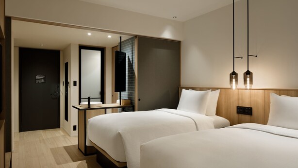 Una habitación de hotel moderna con dos camas, un cabecero de madera, una mesita y un espejo.