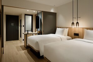 Una habitación de hotel moderna con dos camas, un cabecero de madera, una mesita y un espejo.