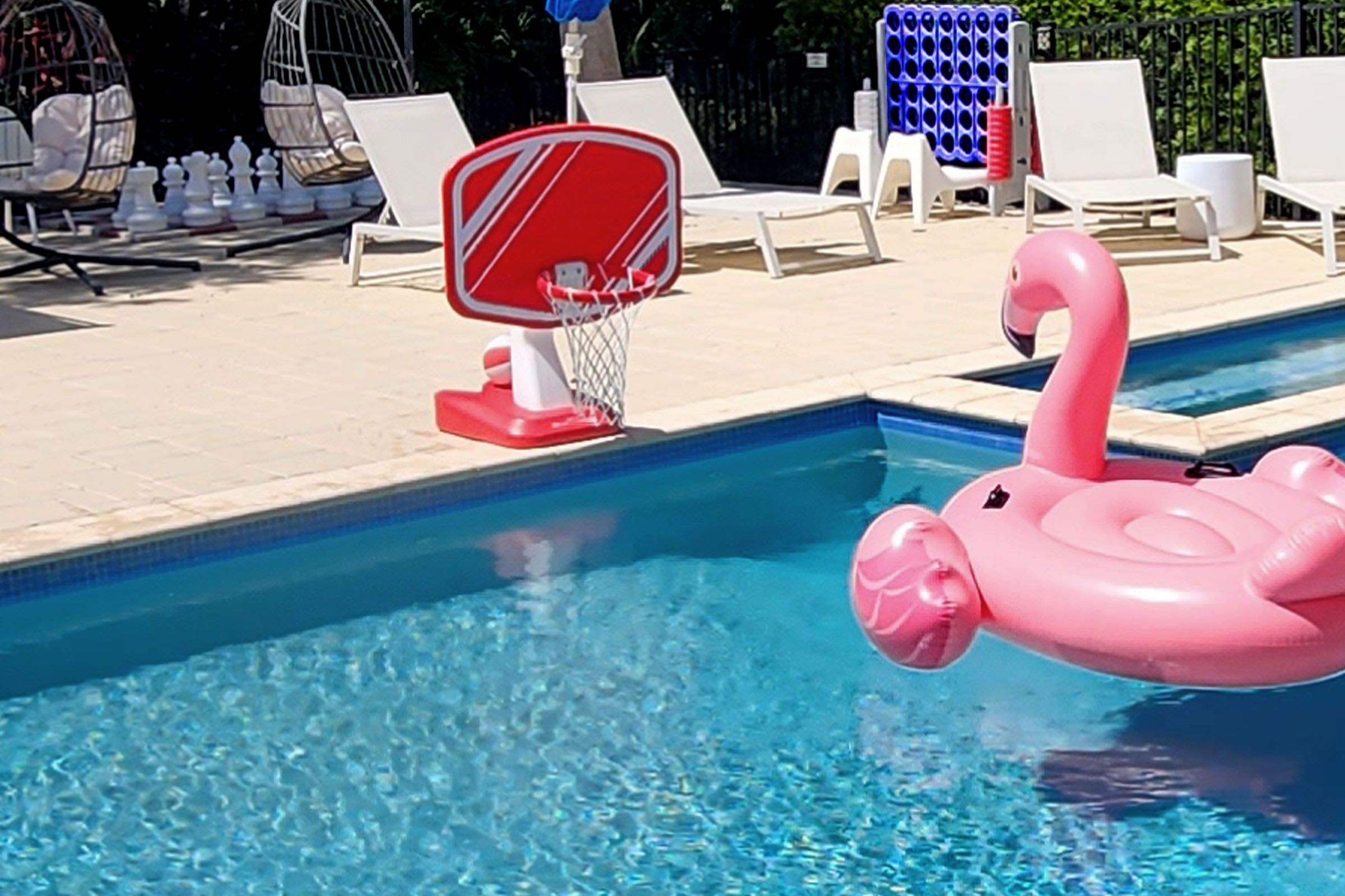 Een zwembad met een roze flamingo drijver en een basketbalring.