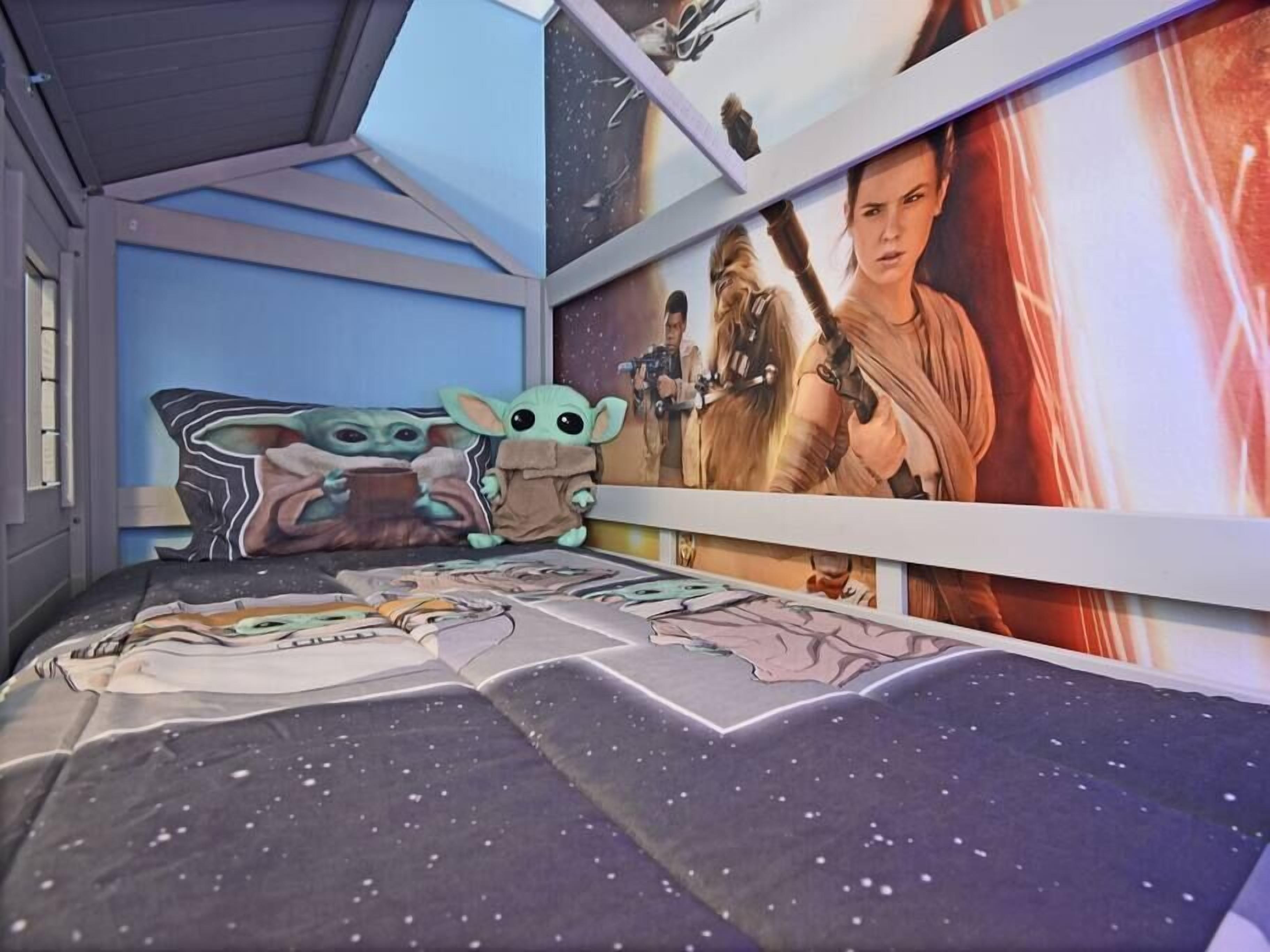 Une chambre à coucher avec une couette, des oreillers et des décorations murales sur le thème de Star Wars, représentant des personnages de la série.