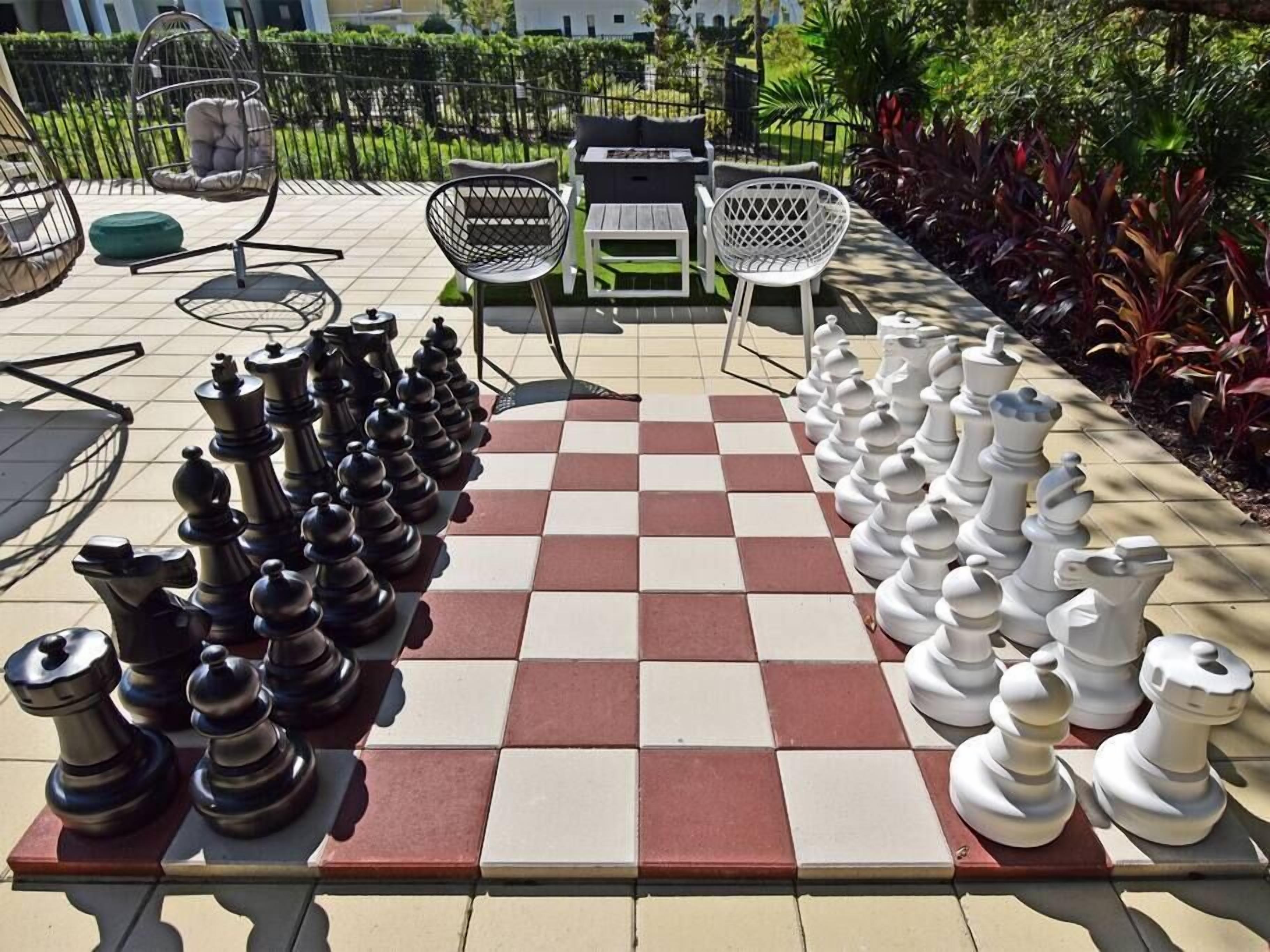 A chessboard set up outdoors with chairs and tables in the background.