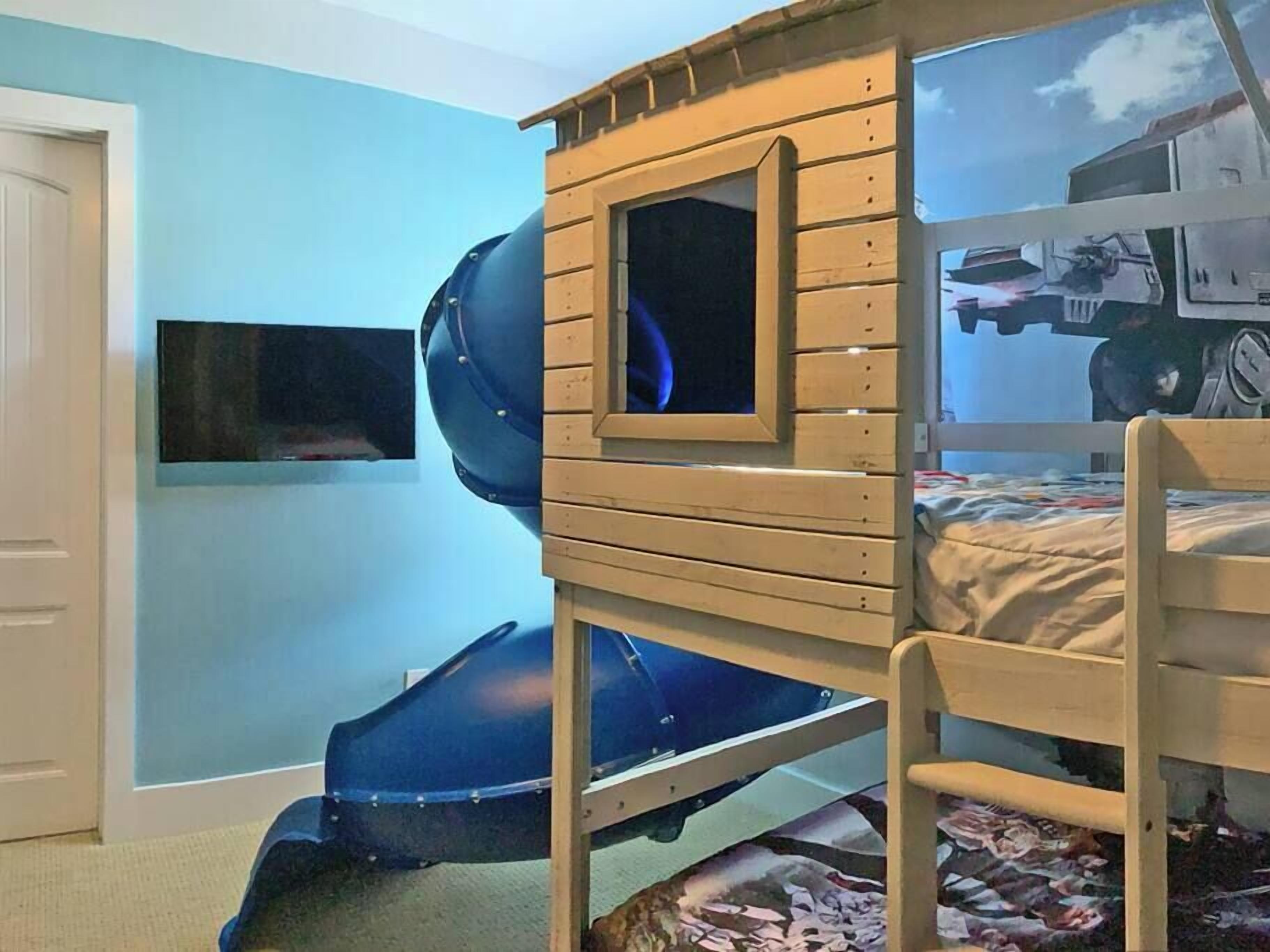 Een stapelbed met een glijbaan en een televisie aan de muur, plus een poster van een voertuig.