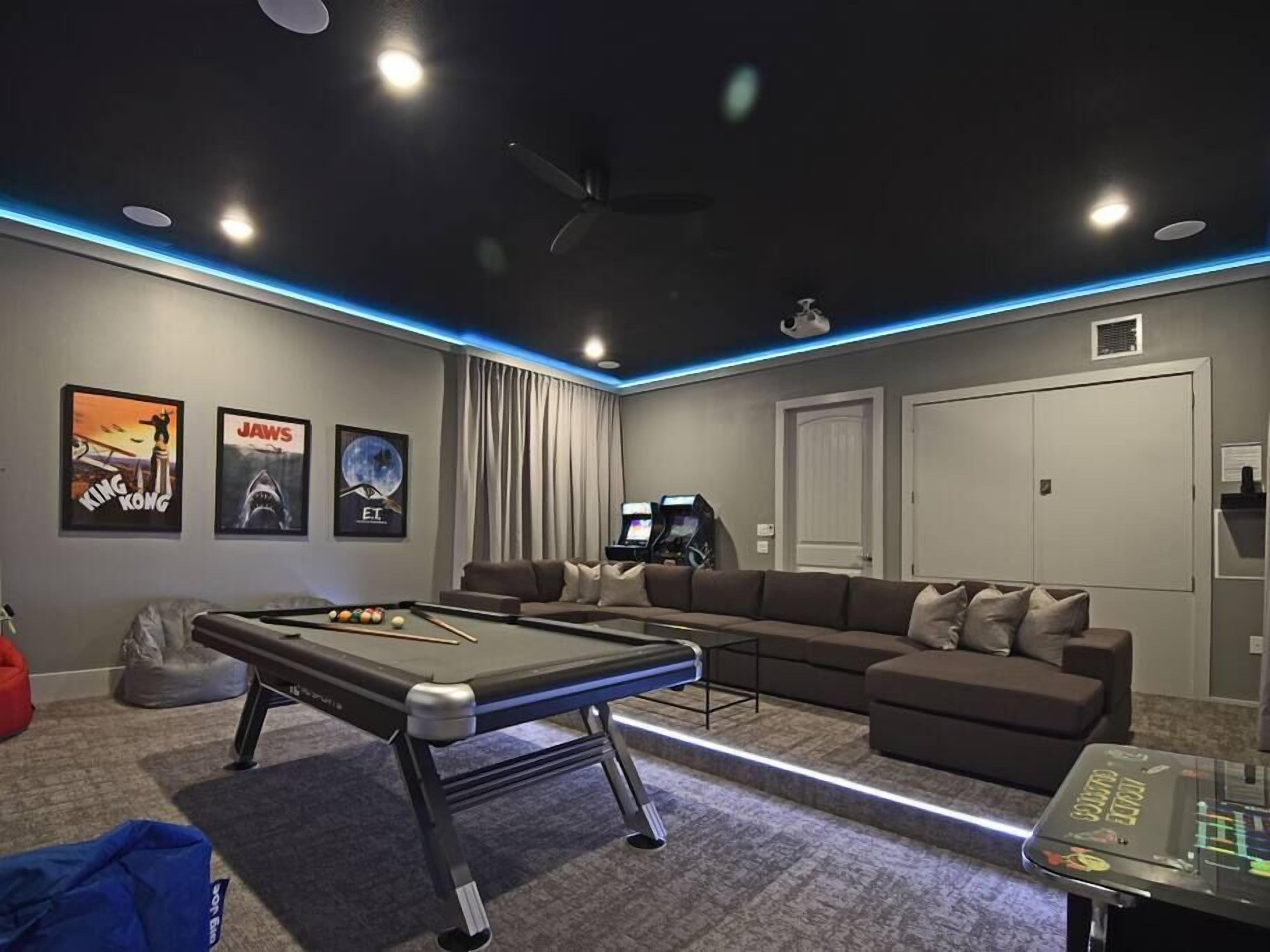 Un salon moderne équipé d’une table de billard, d’un canapé et de deux consoles de jeux.