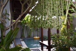 A pool area with a floating ring, surrounded by lush greenery and wooden structures. - Puri Purnama (Kerobokan)