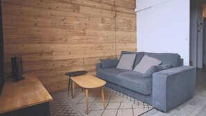 A modern living room with a wooden wall, a grey sofa, a wooden coffee table, and a black lamp. - Studio cabin 4/5 pers, south-facing balcony, TV, equipped kitchen, ski locker (Piau-Engaly)