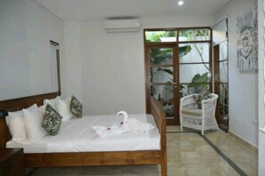 A bedroom with a wooden bed, white bedding, and a swan-shaped towel. There is a chair with a floral cushion near a glass door leading outside.