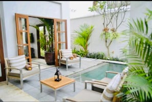 A poolside area with two lounge chairs, a wooden table, and a potted plant.