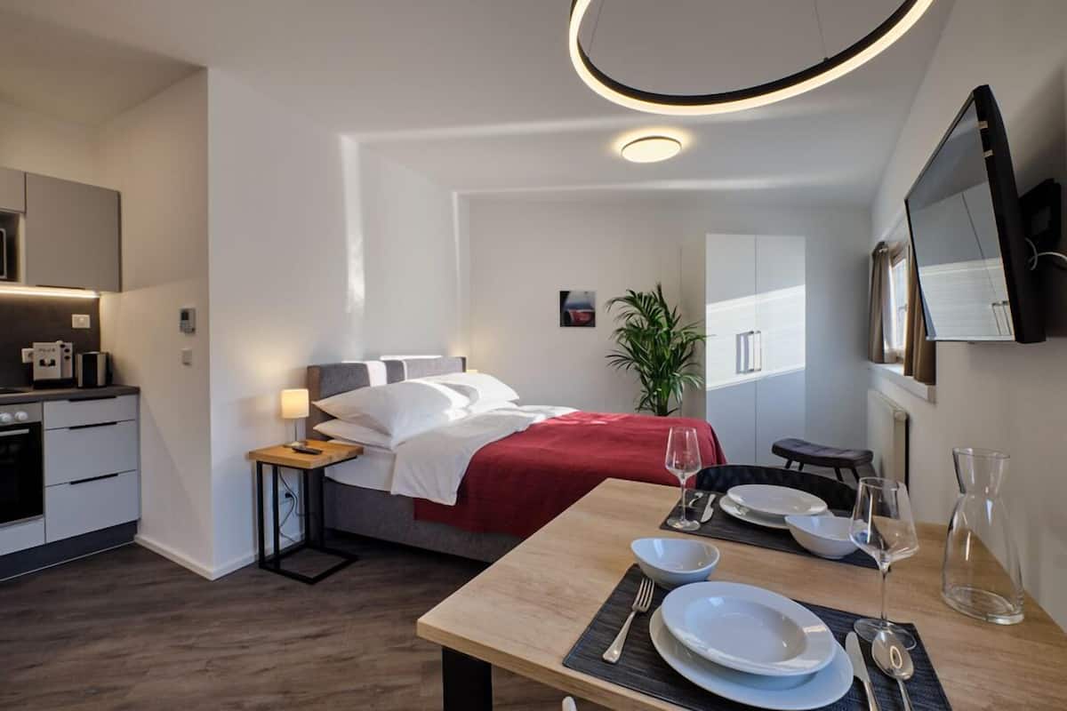 A modern hotel room with a bed, bedside table, dining table, and a TV mounted on the wall.
