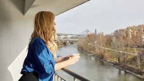 Una persona de pie junto a una barandilla, contemplando un río con un puente al fondo.