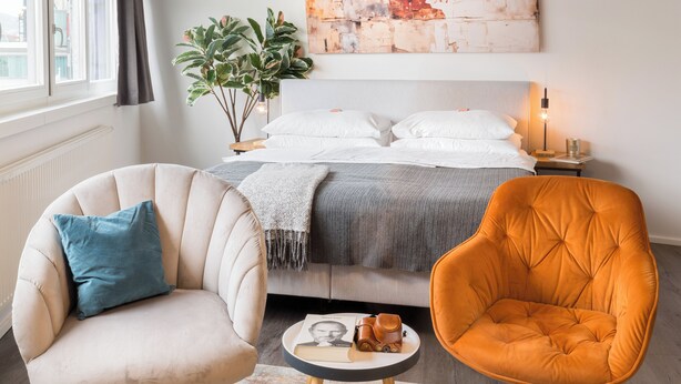 Un dormitorio con una cama, dos sillones, una mesita, una planta y un cuadro en la pared.