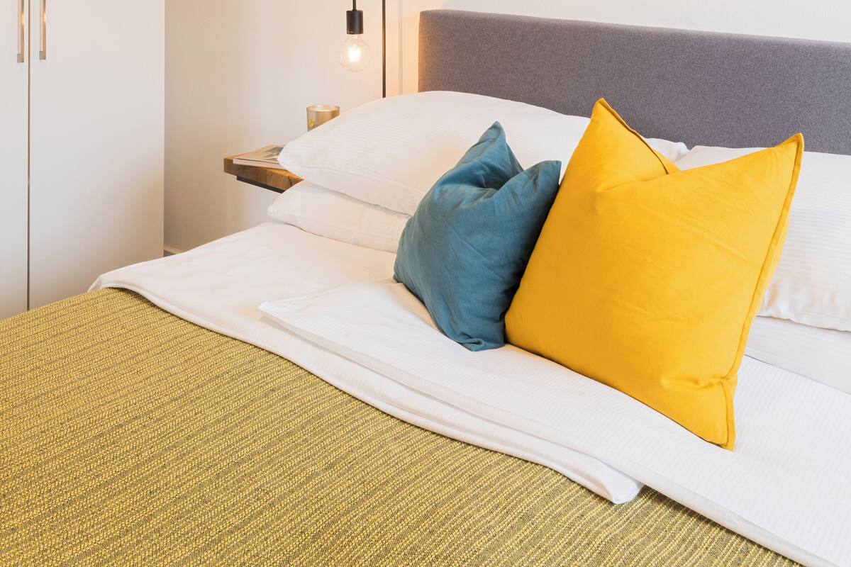 A hotel room with a bed, pillows, a painting on the wall, and a wardrobe.