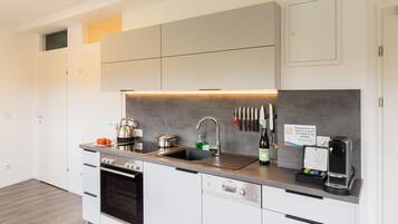 Una cocina moderna con horno empotrado, lavavajillas y fregadero. Se observan unos cuchillos colgados en la pared y un cartel que indica girar el temporizador.