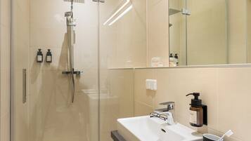 Un baño moderno con ducha de vidrio, dos lavamanos y un espejo grande.