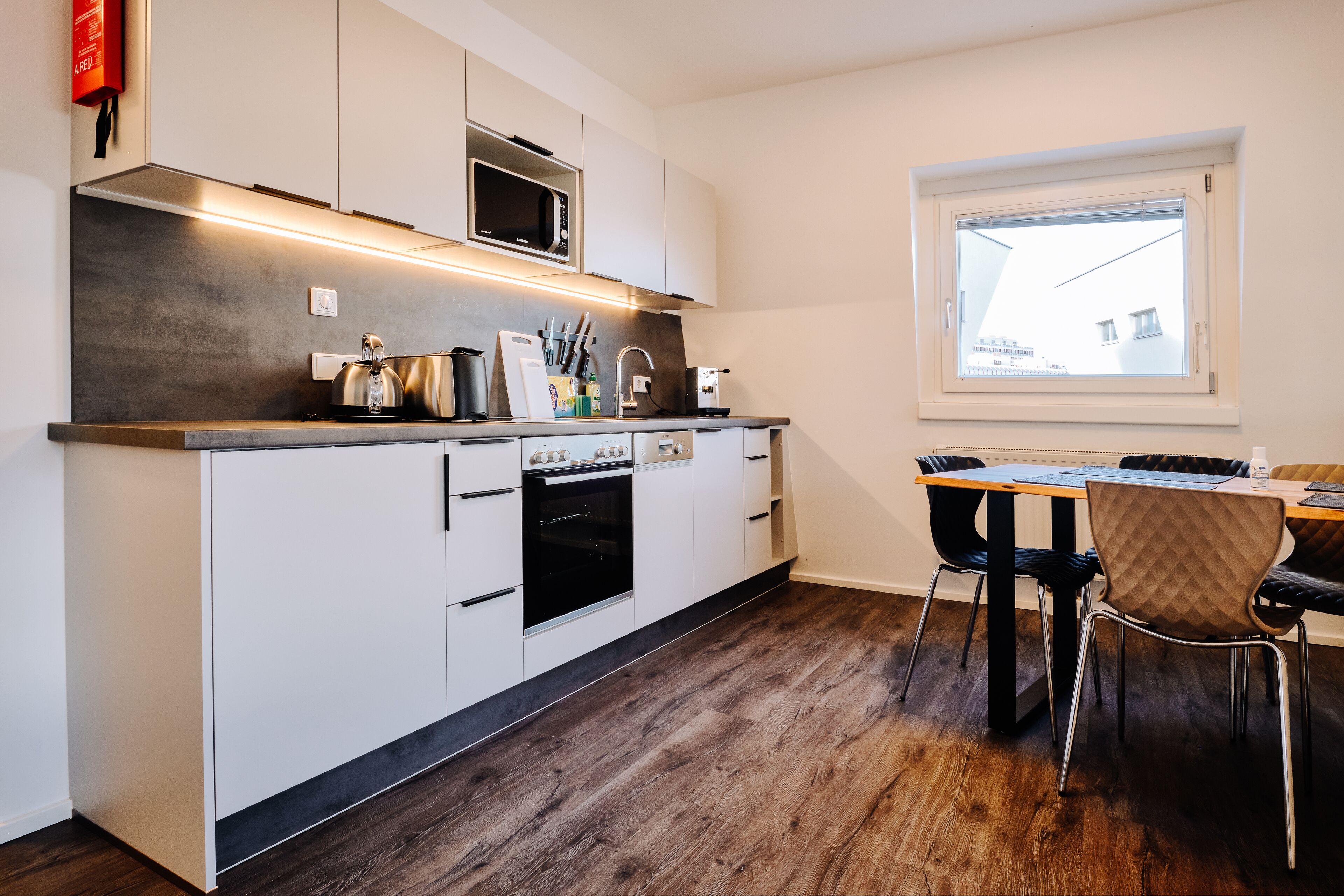 Una cocina moderna con armarios blancos, un microondas, un horno y una zona de comedor con mesa y sillas.