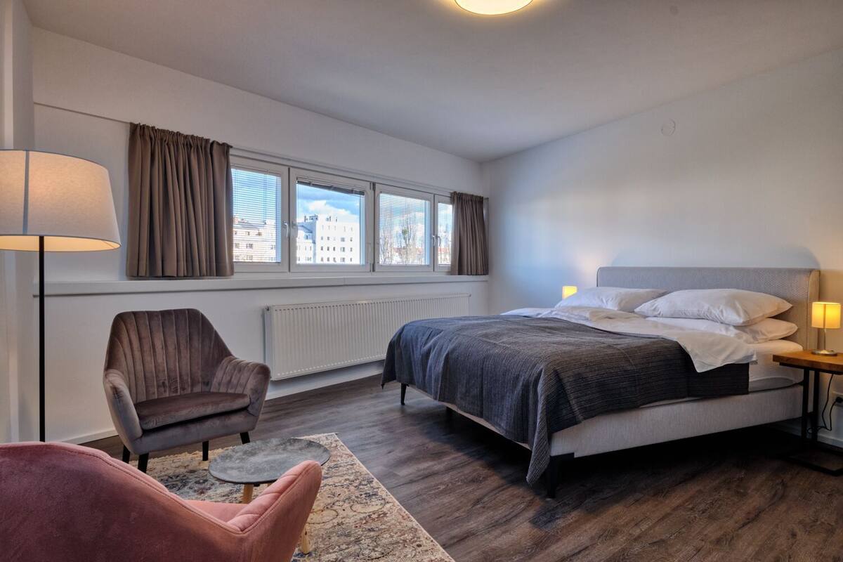 A bedroom with a bed, a chair, a lamp, and a window with curtains.