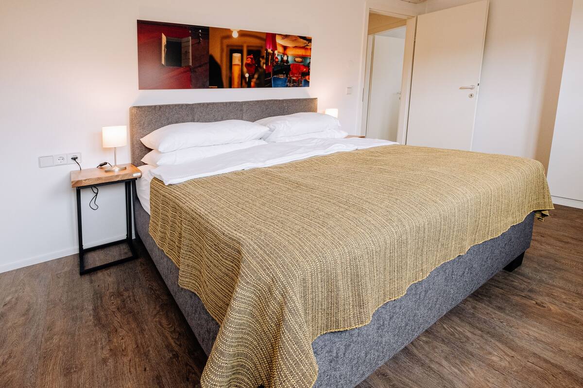 A neatly made bed with a patterned blanket, a bedside table with a lamp, and a wall-mounted artwork above the bed.
