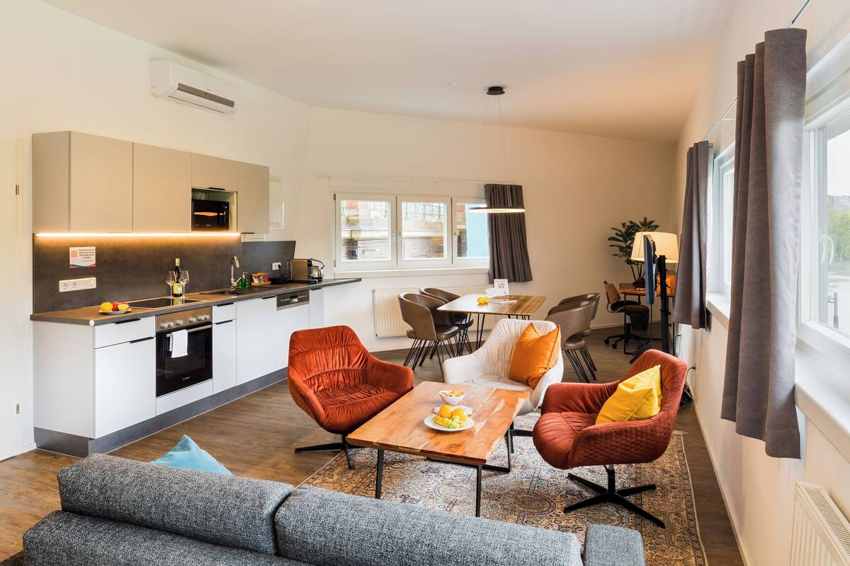 A modern kitchen with a dining area, featuring a sofa, chairs, and a table with a fruit bowl.