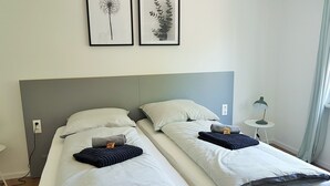 A double bed with white bedding, two pillows, and a blanket. There are two framed pictures on the wall above the bed. - Glück Auf Appartements Walter-Hohmann (Essen)