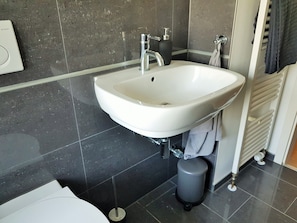 A modern bathroom with a white sink, dark tiled walls, and a towel rack.
