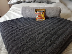 A bed with a grey blanket, a pillow, and a Haribo Goldbären package.