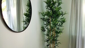 A room with a wooden floor, a white wall, a round mirror, and a tall potted plant. - Glück Auf Appartements Walter-Hohmann (Essen)