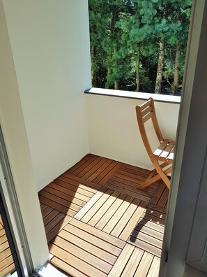 A balcony with wooden flooring and a wooden chair.