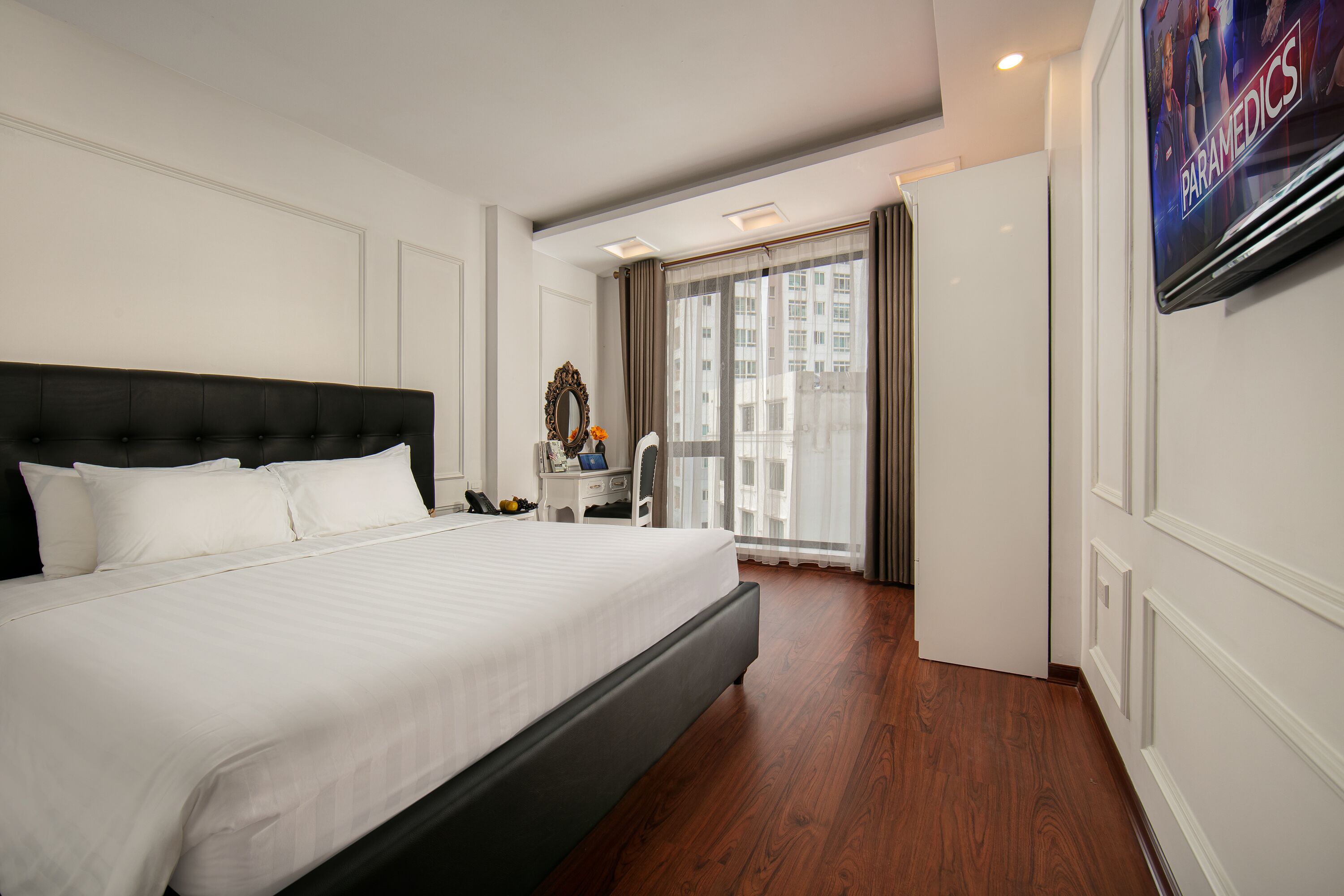 A hotel room with a large bed, a desk, a chair, a TV, and a window with curtains.