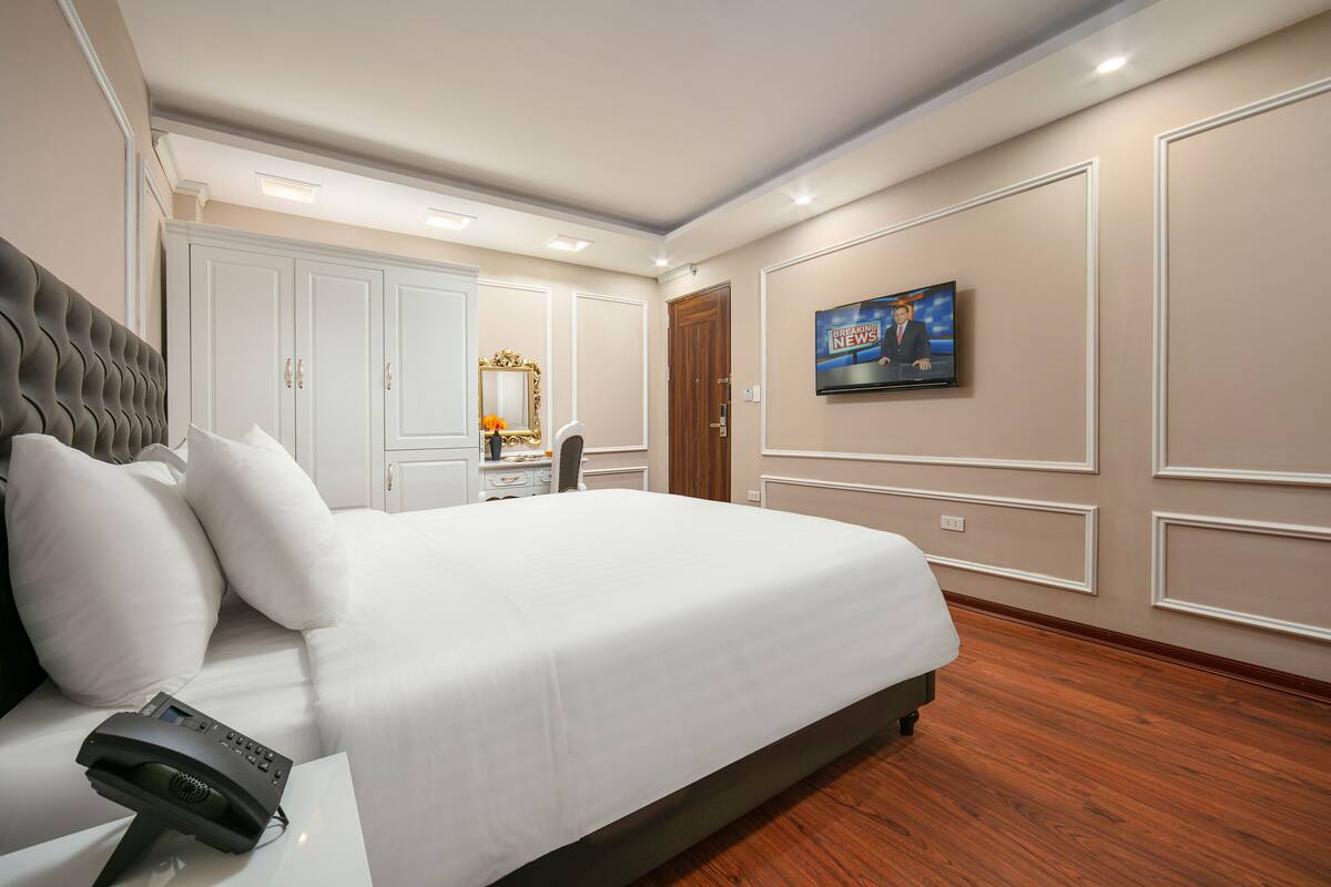 Una habitación de hotel moderna con una cama grande, un televisor montado en la pared y un armario con espejo.