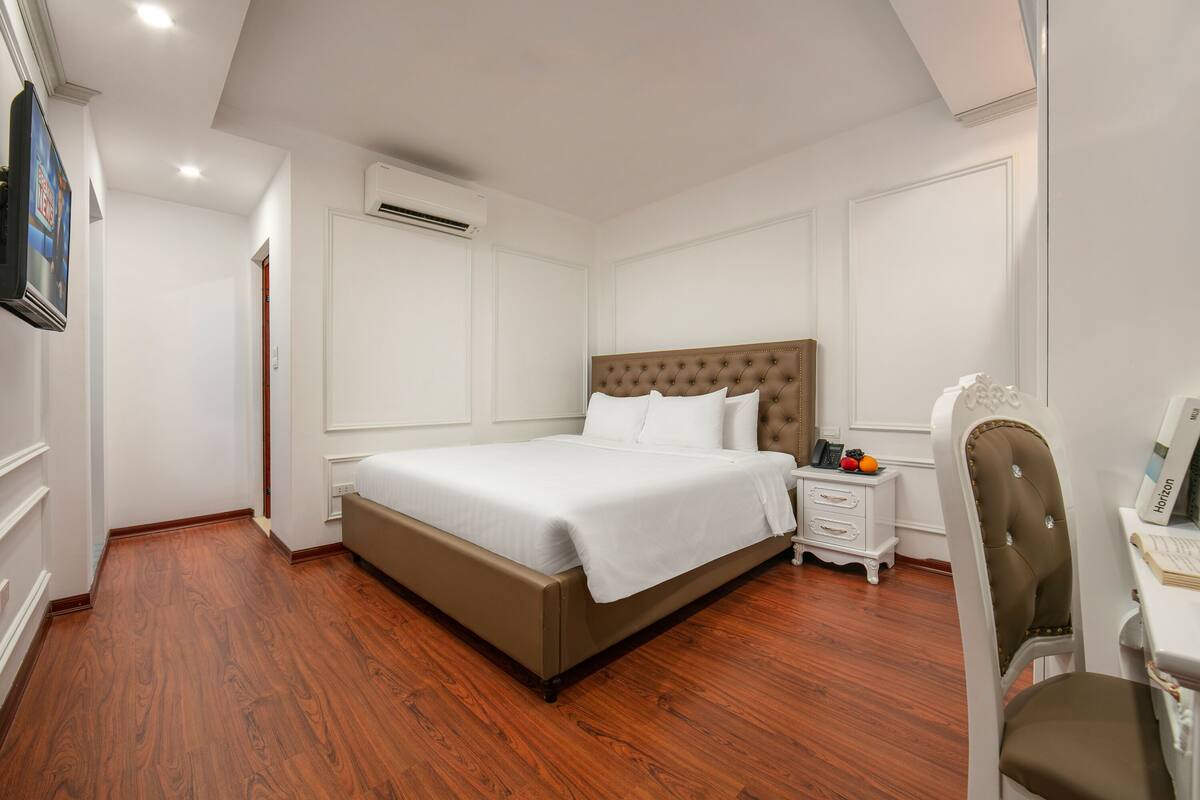 Un dormitorio con cama, mesita de noche, silla y escritorio con computadora.