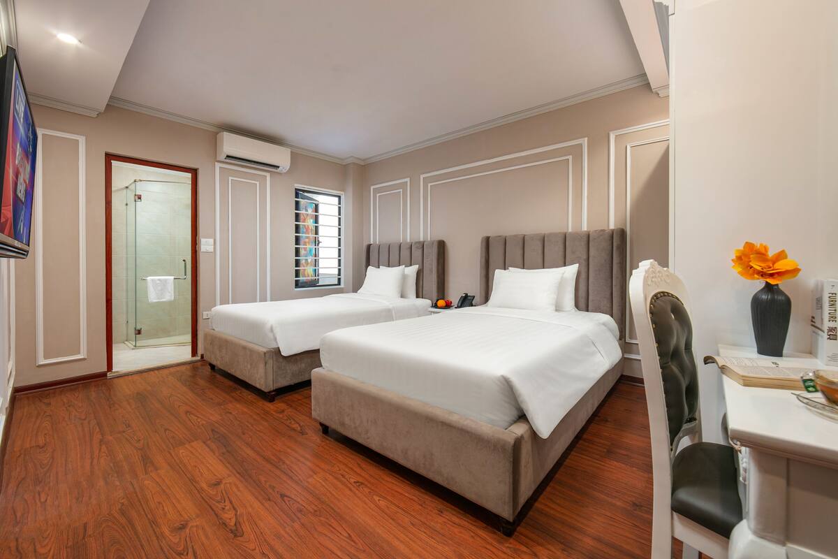 Habitación de hotel con dos camas, un escritorio con silla, televisión y ventana con vistas al exterior.