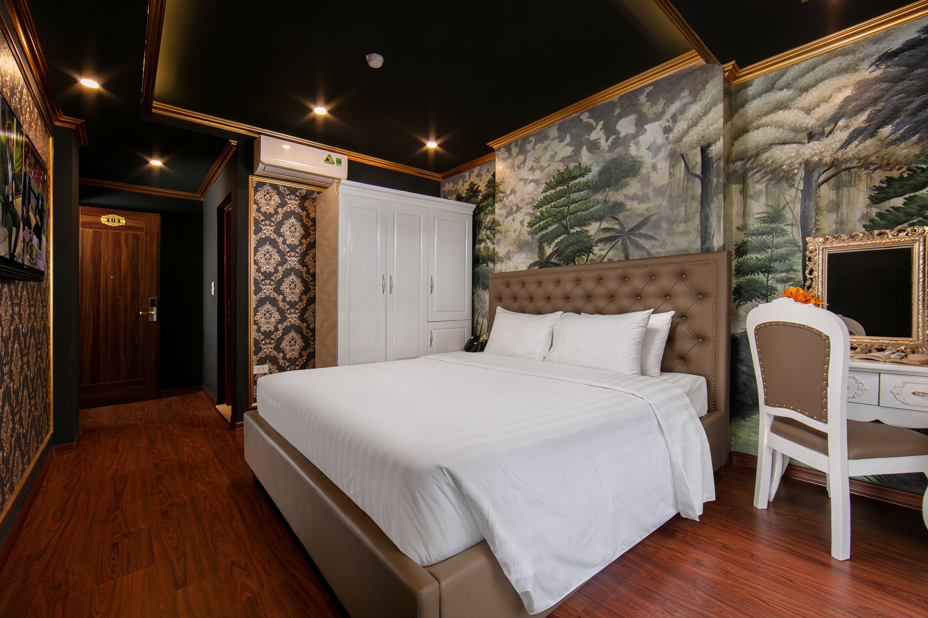 Une chambre avec un grand lit, un bureau et une chaise. On y trouve une armoire et une porte avec une pancarte.