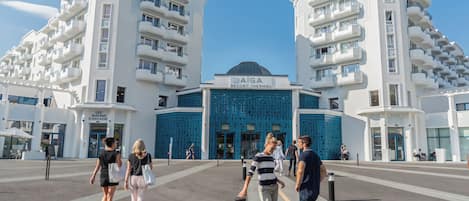 Un hotel moderno con fachada azul central, varios balcones y cielo despejado.
