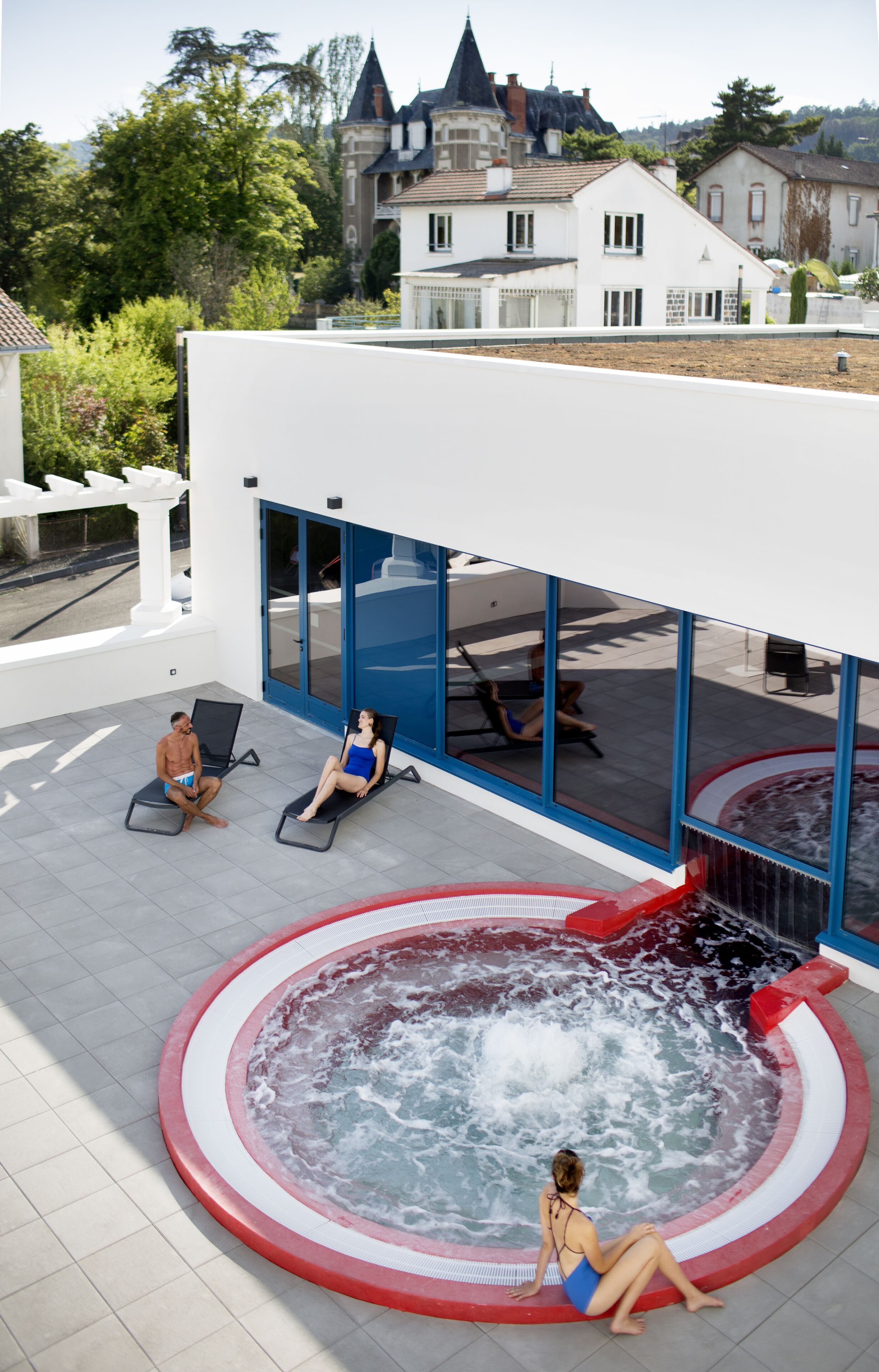 Un espace piscine extérieur moderne, doté d’un jacuzzi, de chaises longues et offrant une vue sur les bâtiments environnants.
