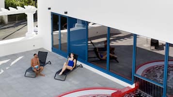 Un espace piscine extérieur moderne, doté d’un jacuzzi, de chaises longues et offrant une vue sur les bâtiments environnants.